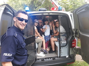 Dzieci w radiowozie policyjnym, przy którym stoi policjant