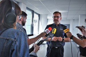 Inspektor Dominik Łączyk podczas udzielania wywiadu. Widoczni dziennikarze, którzy trzymają urządzenia rejestrujące dźwięk.
