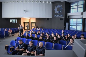 Zdjęcie z oddali. Widoczni policjanci i uczniowie klas mundurowych, którzy siedzą w auli.
