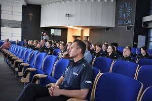 Policjanci i młodzież szkolna siedzą na krzesłach w auli.