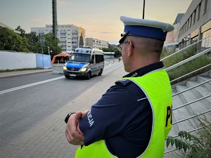 policjant drogówki stoi na chodniku, drogą przejeżdża oznakowany radiowóz