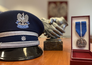 policyjna czapka, obok medal, w tle widać statuetkę złączonych dłoni i Godło Polski