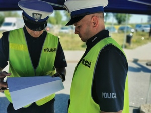 2 policjantów stoi na drodze i patrzą w rozłożony segregator z kartkami
