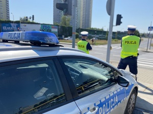 2 policjantów stoi przed radiowozem - fotografujący stoi za pojazdem
