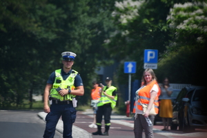zdjęcie kolorowe: policjant drogówki i wolontariusze zabezpieczający przejazd kolarzy na terenie Katowic