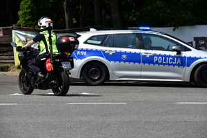 zdjęcie kolorowe: policyjny radiowóz i pilot wyścigu na motocyklu