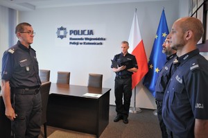 Komendant Wojewódzki Policji w Katowicach, Naczelnik Wydziału Kadr oraz policjanci, którzy wzięli udział w uroczystości. Wszyscy umundurowani, w tle flagi Polski i Unii Europejskiej.
