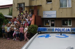 Na zdjęciu przed budynkiem widać wszystkich uczestników spotkania wraz z opiekunem i policjantami, po prawej stronie zaparkowany oznakowany radiowóz policyjny.