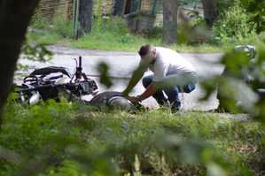 Zdjęcie wykonane z ukrycia. Na fotografii widać mężczyznę, który sprawdza co się stało motocykliście.