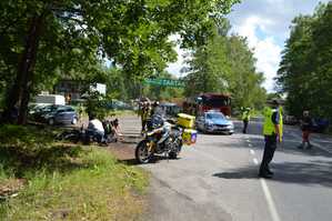 zdjęcie z miejsca symulowanego wypadku motocyklisty. Na zdjęciu widoczni policjanci, radiowóz oraz ratownik medyczny na motocyklu.