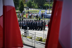 Na pierwszym planie flagi Polski, w tle policjanci biorący udział w uroczystości.