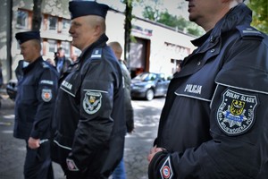 Na zdjęciu występuje trzech policjantów umundurowanych, z prawej strony wyraźnie widać tarcze z oznaczeniem Komendy Wojewódzkiej z Dolnego Śląska. Wszyscy policjanci stoją przed budynkiem kopalni.
