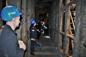 Na zdjęciu widać wnętrze kopalni pod ziemią (korytarz pootrzymywany drewnianymi belkami) oraz 3 policjantów umundurowanych oraz kilka osób innych służb w kaskach ochronnych biorących udział w ćwiczeniach.