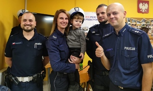 Na zdjęciu widocznych jest trzech policjantów i policjantka trzymająca na rękach dziecko w czapce policjanta ruchu drogowego.