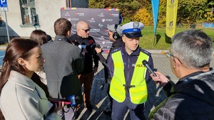 policjant udzielający wywiadu dziennikarzom podczas inauguracji akcji. W tle kierowca rajdowy Jarosław Szeja.