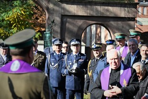 Zdjęcie przedstawia przedstawicieli służb mundurowych oraz duchownych na cmentarzu