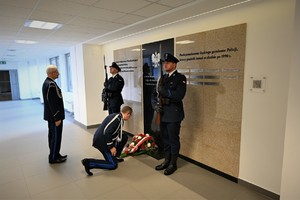 zdjęcie przedstawia Komendanta Wojewódzkiego składającego wieniec pod tablicą pamiątkową w asyście honorowej dwóch policjantów