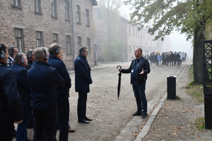 przewodnik przeprowadzający prelekcje na terenie obozu Auschwitz. W tle inna grupa zwiedzających.