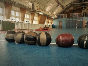 zdjęcie przedstawia piłki lekarskie leżące w rzędzie na podłodze hali sportowej