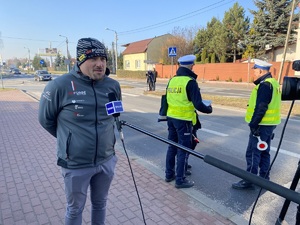 kierowca rajdowy Jarosław Szeja udzielający wywiadu dla telewizji. W tle policjanci ruchu drogowego.
