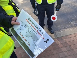 policjant ruchu drogowego trzymający kartkę z tekstem &quot;Światowy Dzień Pamięci Ofiar Wypadków Drogowych 20 listopada 2022r.&quot;