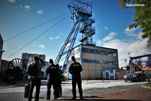 Zdjęcie. Umundurowani policjanci na terenie kopalni, w tle widoczny wyciąg szybu