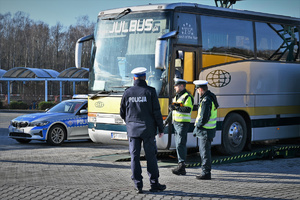 Na zdjęciu policjant oraz funkcjonariusze inspekcji transportu drogowego stoją przy autokarze.