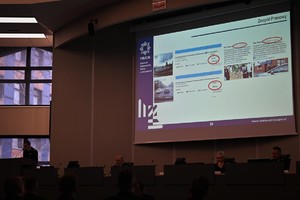 Zdjęcie przedstawia przemawiającego Komendanta Wojewódzkiego Policji, w tle widoczny ekran z wyświetloną prezentacją