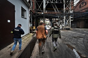 Zdjęcie przedstawia dwóch nieumundurowanych policjantów idących z pracownikiem kopalni po jej terenie