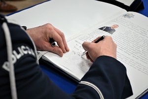 Zdjęcie przedstawia zastępcę komendanta wojewódzkiego dokonującego wpisu w księdze pamiątkowej