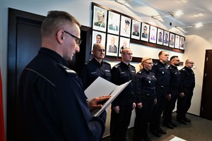 Zdjęcie przedstawia policjanta odczytującego rozkazy personalne, w tle policjanci stojący w szeregu.