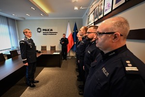 zdjęcie przedstawia zbliżenie na Komendanta, w tle stojący w szeregu policjanci oraz policjant odczytujący rozkazy personalne.