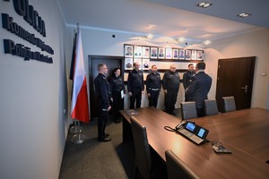 Zdjęcie przedstawia gabinet. W tle widać policjantów stojących w szeregu.