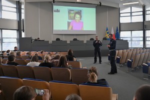 Zdjęcie. Widoczni uczestnicy briefingu oraz prowadzący, a także ambasadorka briefingu na ekranie podczas połączenia video