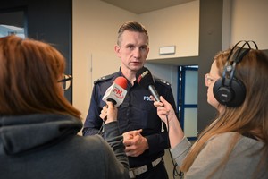 Zdjęcie. Policjant wypowiadający się przed mikrofonami dziennikarzy