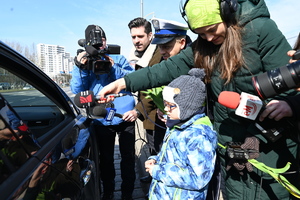 zdjęcie kolorowe przedstawiające kontrolę pojazdu przez policjanta z drogówki wraz z przedszkolakiem, wokoło dziennikarze z aparatami i mikrofonami