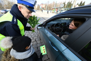zdjęcie kolorowe przedstawiające policjanta z dziewczynką przy samochodzie w którym za kierownicą siedzi kobieta