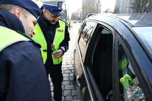 zdjęcie kolorowe przedstawiające dwóch policjantów, jeden trzyma w ręku tulipana, stojących przy samochodzie i rozmawiających z kierowcą
