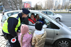 zdjęcie kolorowe przedstawiające policjanta z przedszkolakami przy samochodzie w którym siedzą dwie kobiety