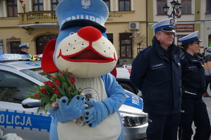 Sznupek trzyma kwiaty obok stoją policjanci w tle rynek miasta zdjęcie kolorowe zrobione na zewnątrz
