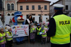 policjant stoi tyłem i rozmawia z dziećmi koło dzieci stoi miss polski w tle rynek
