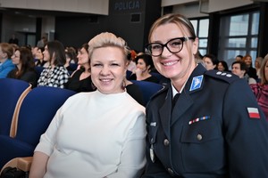 zdjęcie kolorowe w auli komendy, zdjęcie siedzących kobiet, na pierwszym planie pracownica policji i policjantka w mundurze