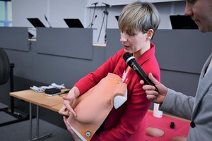 zdjęcie kolorowe w auli komendy, kobieta prezentująca na manekinie sposób badania piersi