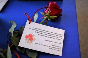 zdjęcie kolorowe w auli komendy, na niebieskim suknie leży róża z przypiętą karteczką o treści &quot;Z okazji Dnia Kobiet składamy Tobie najserdeczniejsze życzenia zdrowia, pomyślności, samych pięknych dni w życiu. Życzymy, aby uśmiech rozpromieniał Twoją twarz, być zawsze czuła się spełniona i doceniana. Z policyjnym pozdrowieniem Funkcjonariusze Gabinetu Komendanta Wojewódzkiego Policji KWP w Katowicach&quot;