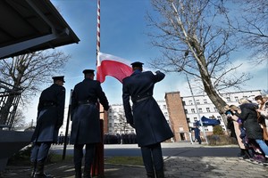 zdjęcie przedstawia trzech policjantów przy maszcie w trakcie podnoszenia flagi państwowej