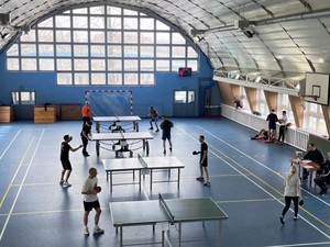 Widok z góry na halę sportową. Na zdjęciu widać zawodników podczas gry w tenisa stołowego.