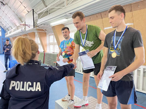 Na zdjęciu widać Zastępcę Naczelnika Wydziału Doboru i Szkolenia KWP w Katowicach podczas składania gratulacji zwycięzcom zawodów stojącym na podium.