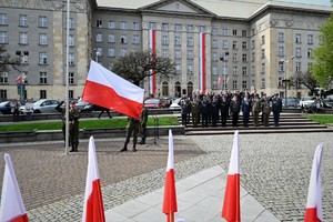 zdjęcie przedstawia poczet flagowy trzymający flagę, w tle przedstawiciele władzy i służb mundurowych
