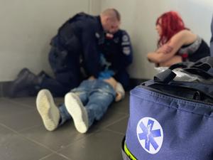 zdjęcie przedstawia zbliżenie na torbę medyczną, w tle policjanci i kobieta ćwiczący na manekinie sztuczne oddychanie.