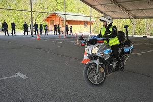 Zdjęcie. Policjant na motocyklu podczas konkurencji jazdy na motocyklu oraz inni umundurowani policjanci